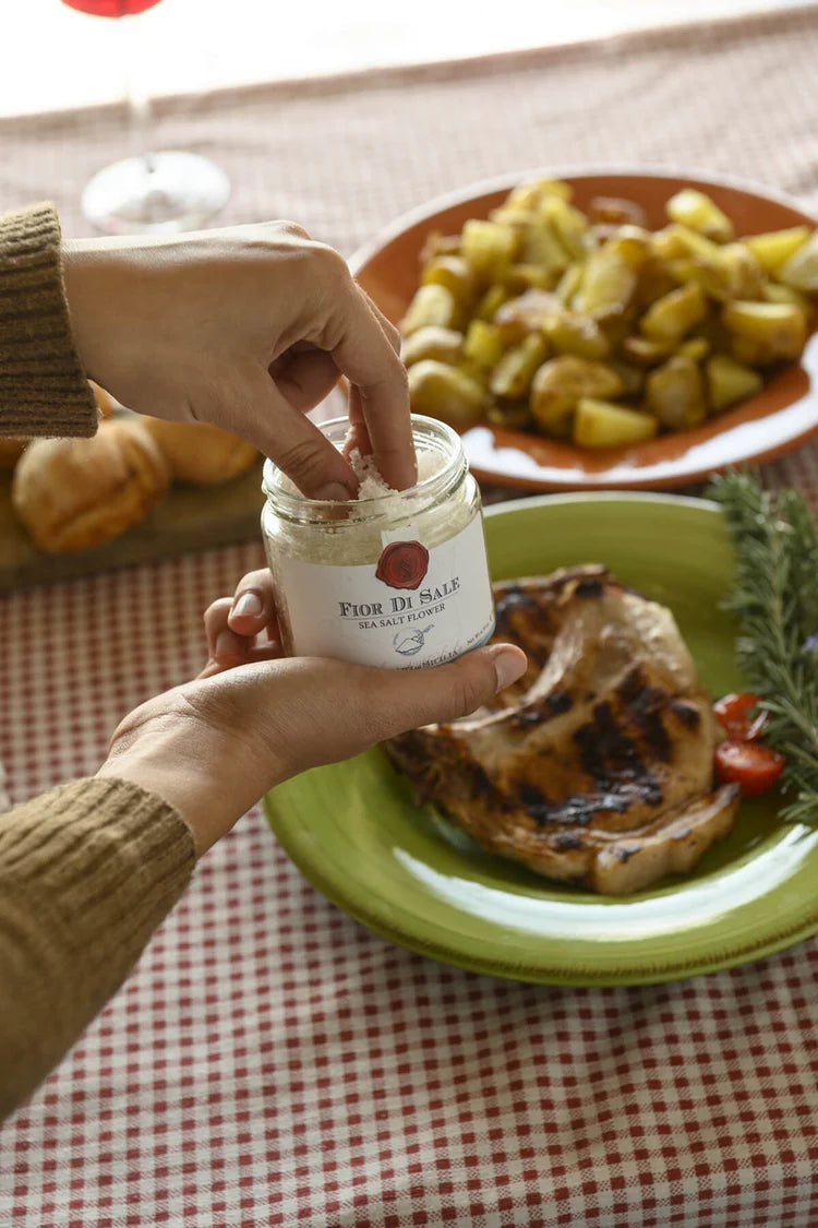 Person holding a jar of jam over a plate with food on a checkered tablecloth